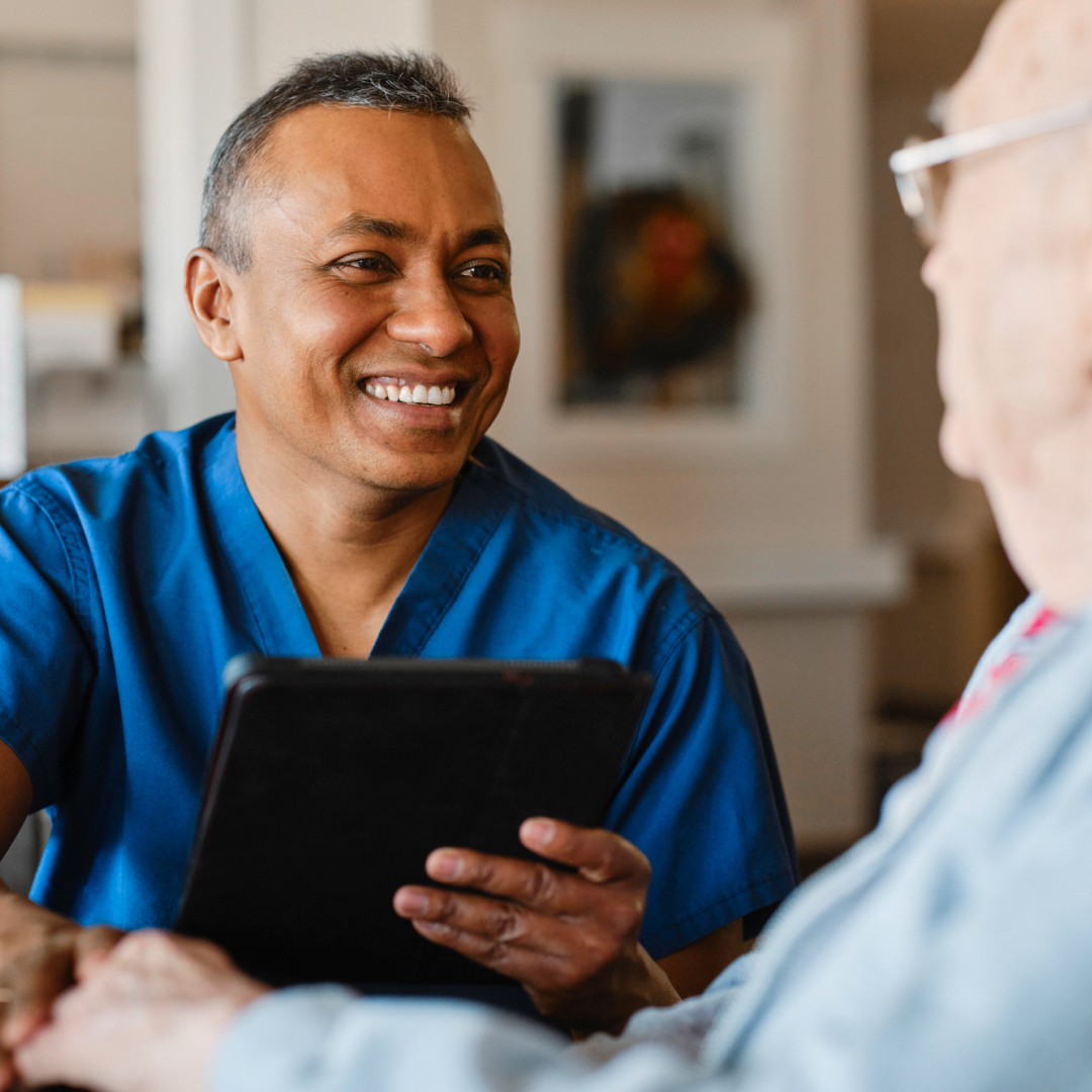 A male nurse holding a tablet and smiling at an older client in a long-term care home.