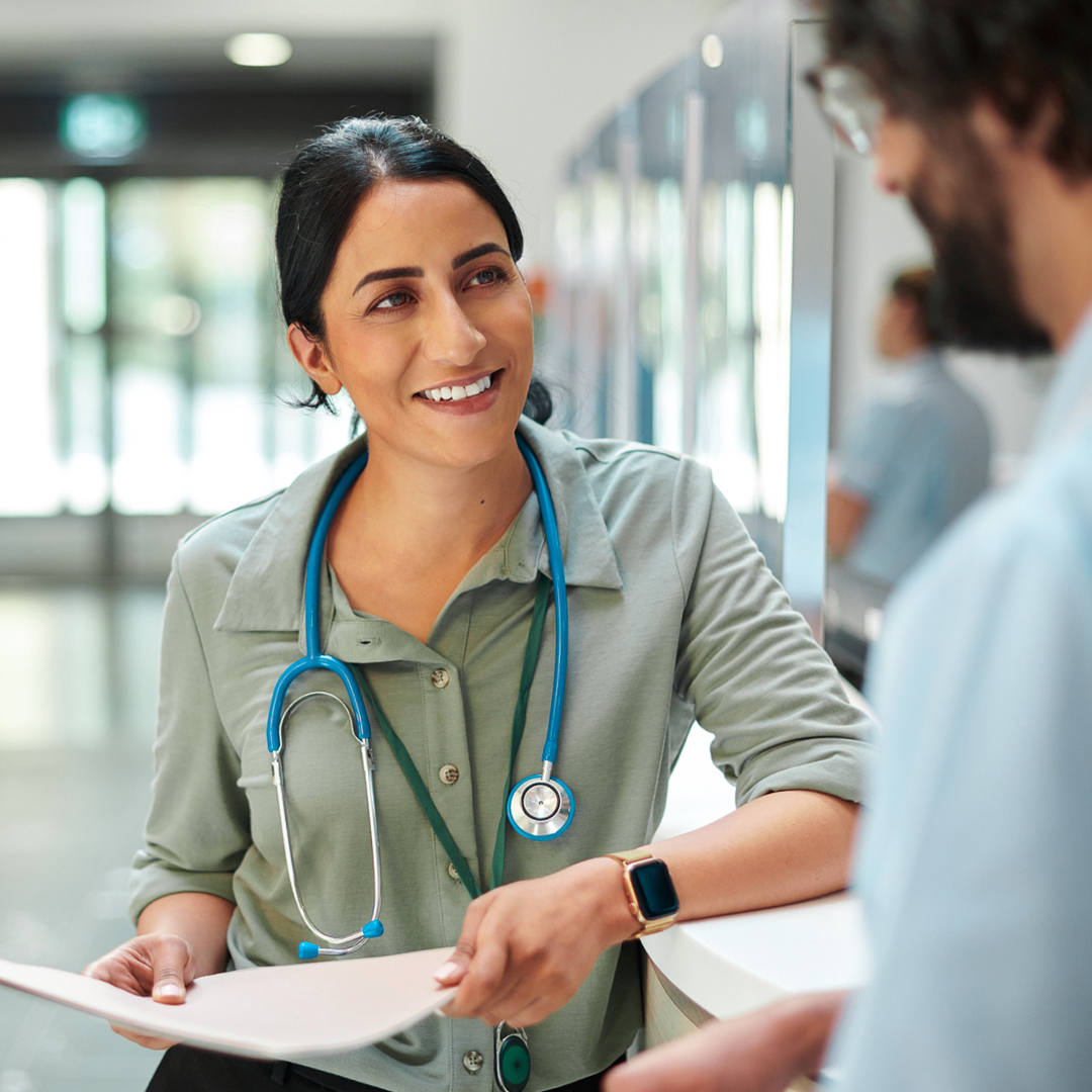 Two nurses having a discussion in a hospital setting. One nurse is holding a manilla folder.