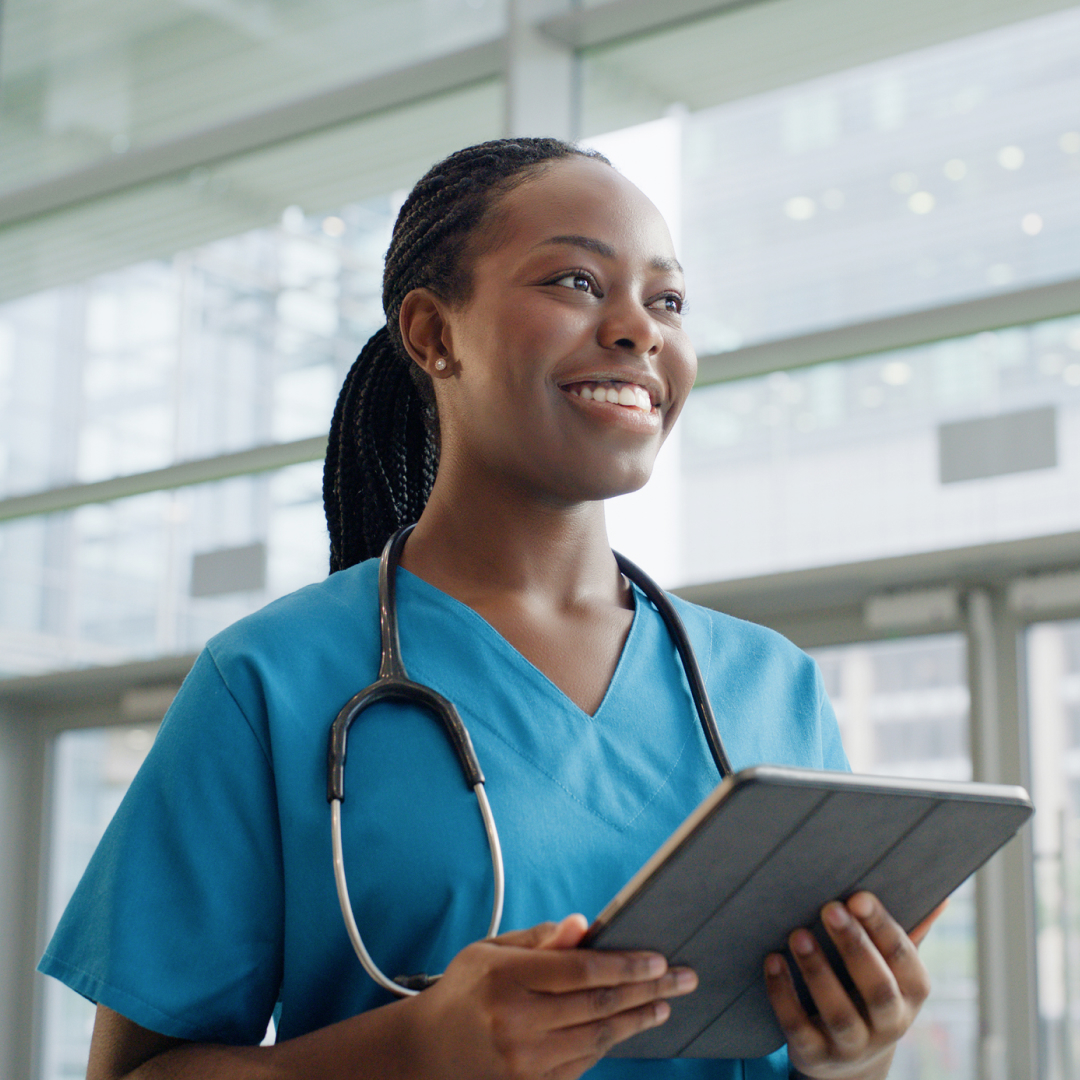 A female nurse looking upwards and smiling while holding a tablet.