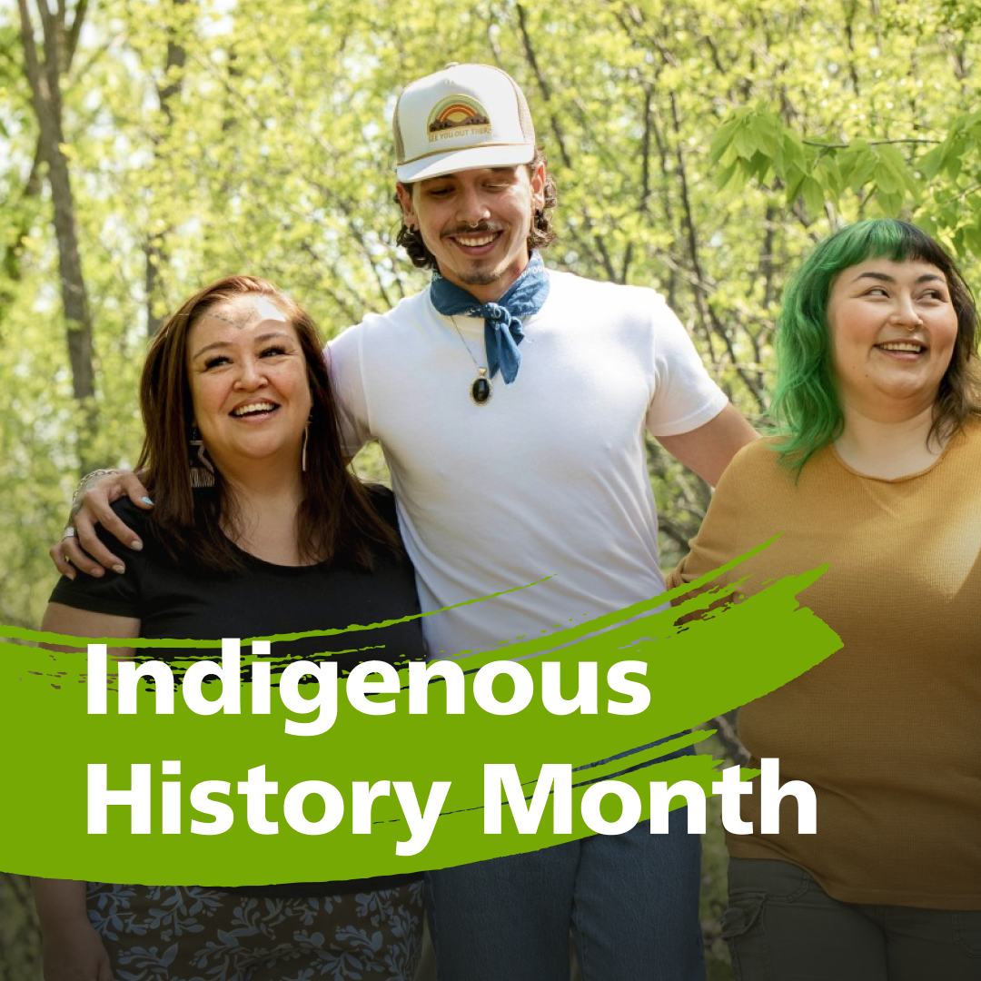 Three smiling Indigenous adults walk together through a forest, with the text “Indigenous History Month” displayed below them.