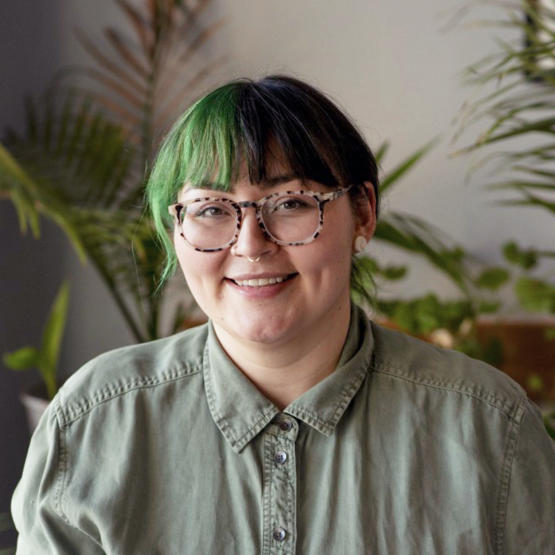 Une personne portant une chemise verte à col boutonné est assise devant un arrière-plan de plantes d'intérieur. Le visage de la personne est flouté. Photo de la banque de photos autochtones de CIRA.