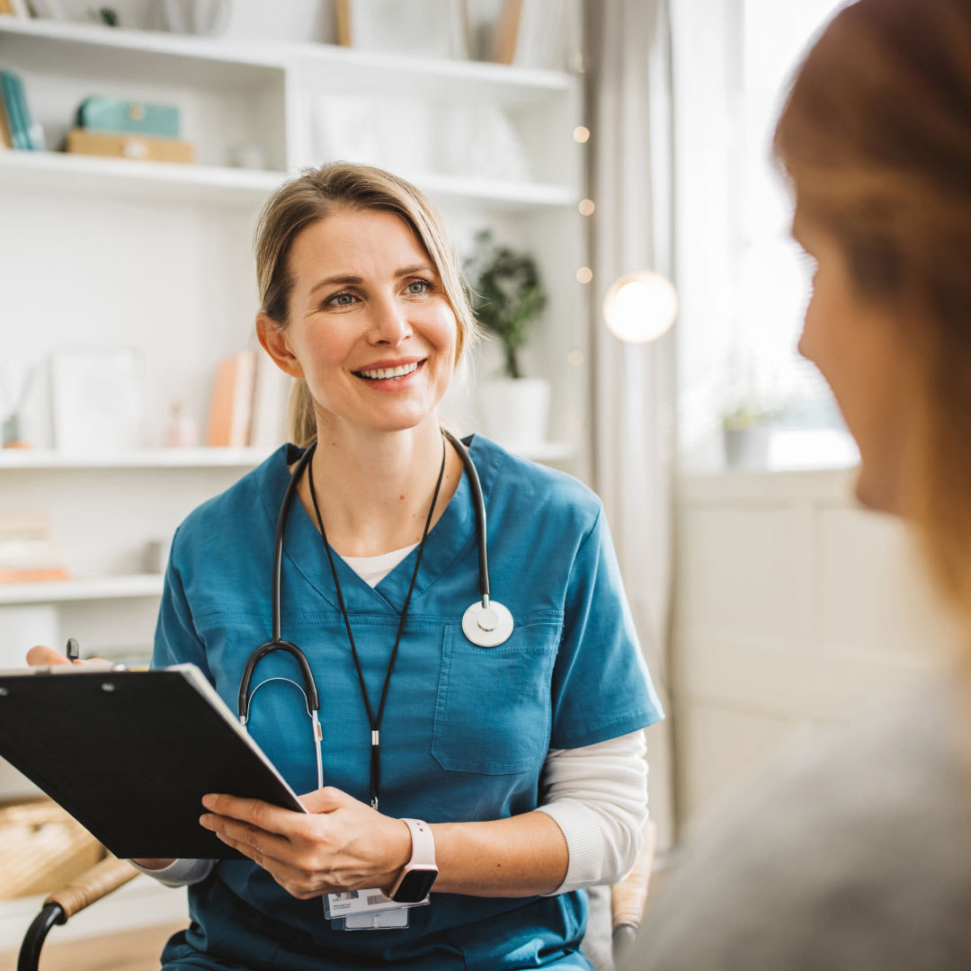 A nurse smiling at patient while writing on a clipboard.