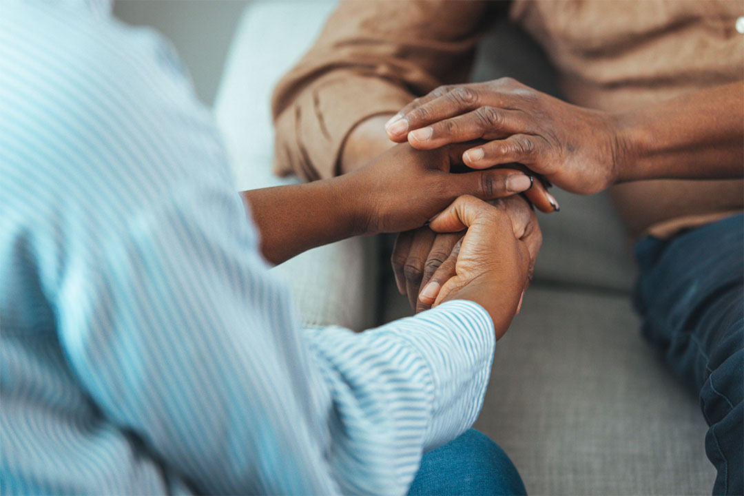 A closeup of two Black individuals sitting closely and holding hands.