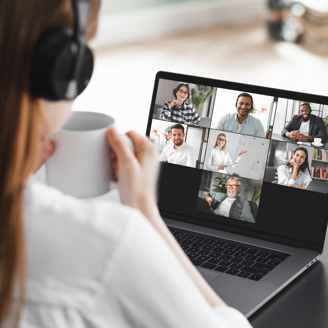 A woman holding a coffee mug while attending a virtual meeting on her laptop.