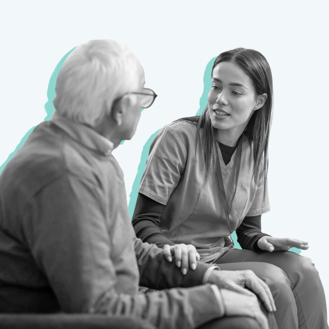 A young nurse talking to an older patient with her hand on his arm.