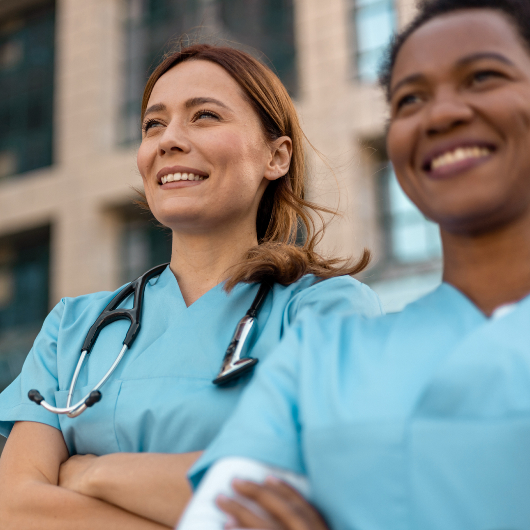 Two nurses with their arms crossed, smiling and looking upwards.
