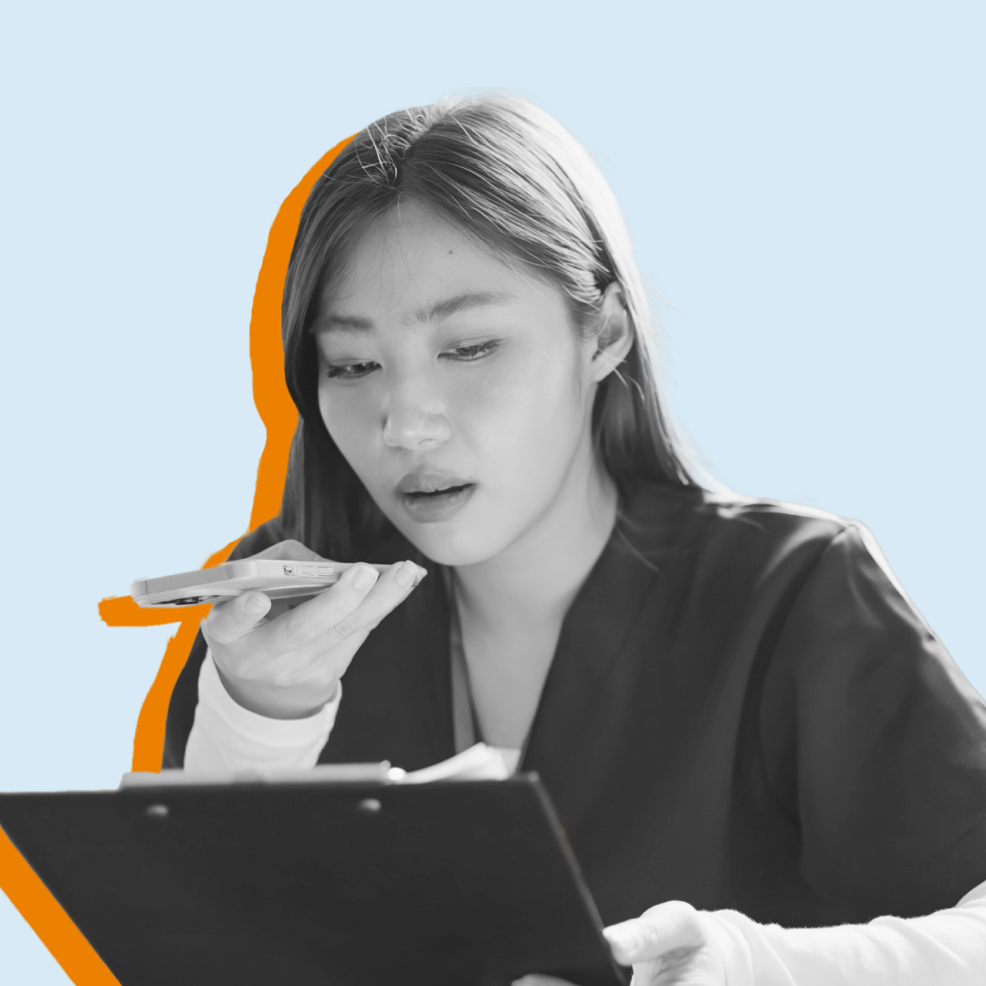 A female nurse speaking into an AI app on a smartphone while looking at patient’s chart.